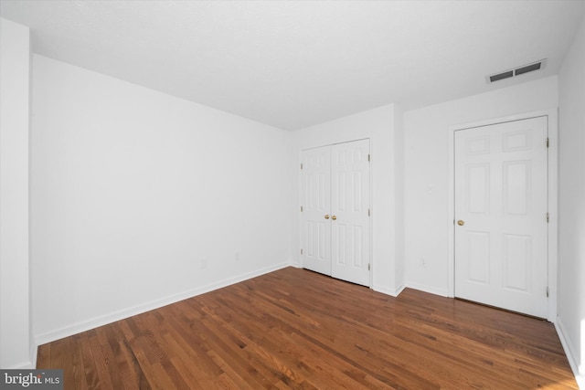 unfurnished bedroom with wood finished floors, visible vents, a closet, and baseboards