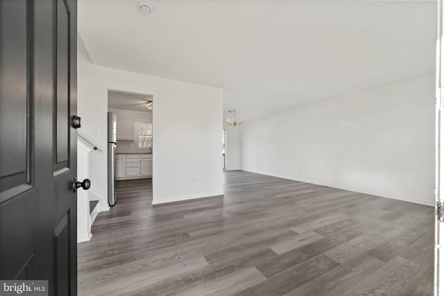 unfurnished room with dark wood-style floors, a chandelier, and baseboards