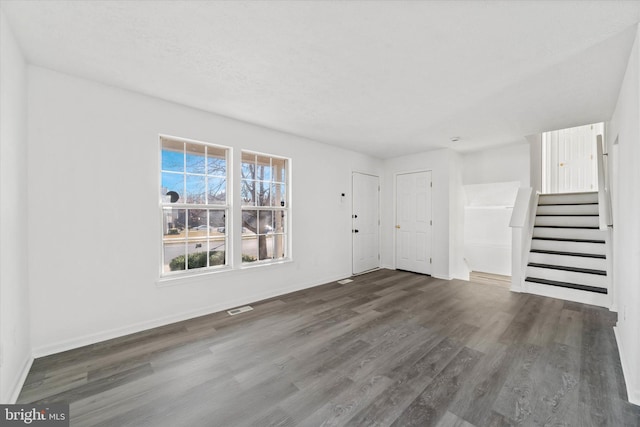 unfurnished living room with visible vents, baseboards, wood finished floors, and stairs