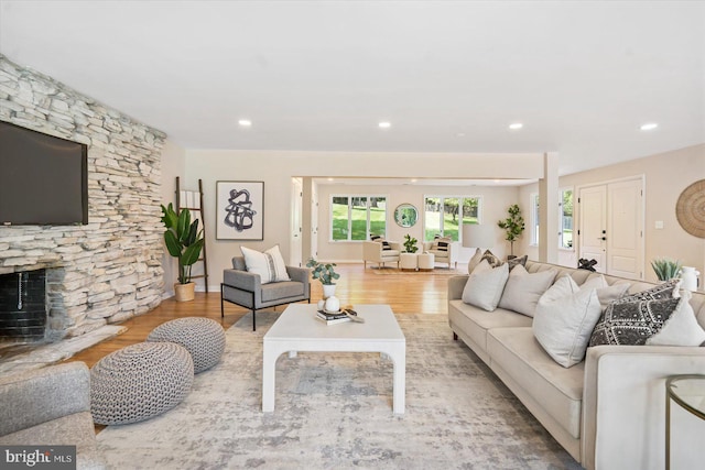 living room featuring a stone fireplace, recessed lighting, and wood finished floors