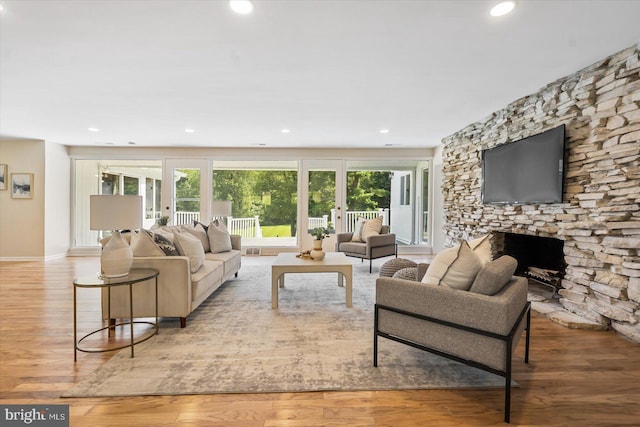 living room featuring recessed lighting, baseboards, a stone fireplace, and wood finished floors