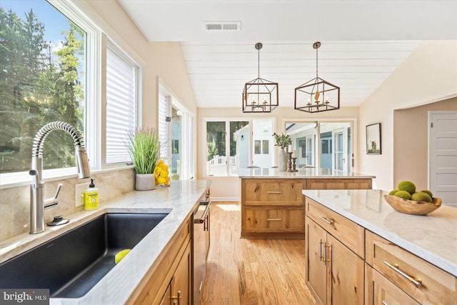 kitchen with visible vents, a sink, light wood finished floors, lofted ceiling, and hanging light fixtures