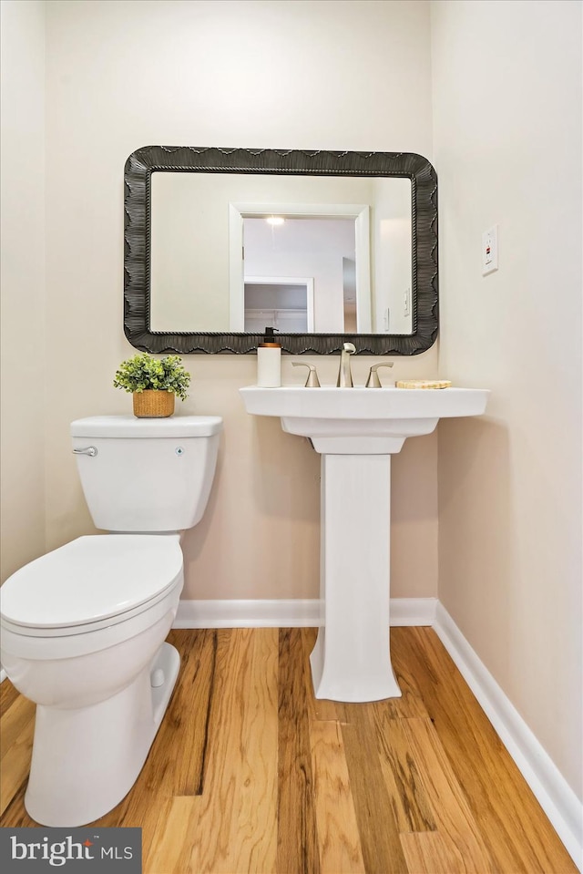 half bath with toilet, baseboards, and wood finished floors