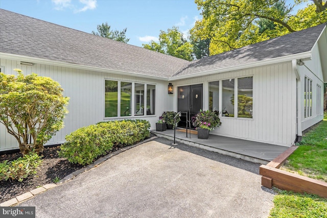 entrance to property with a patio area and a shingled roof