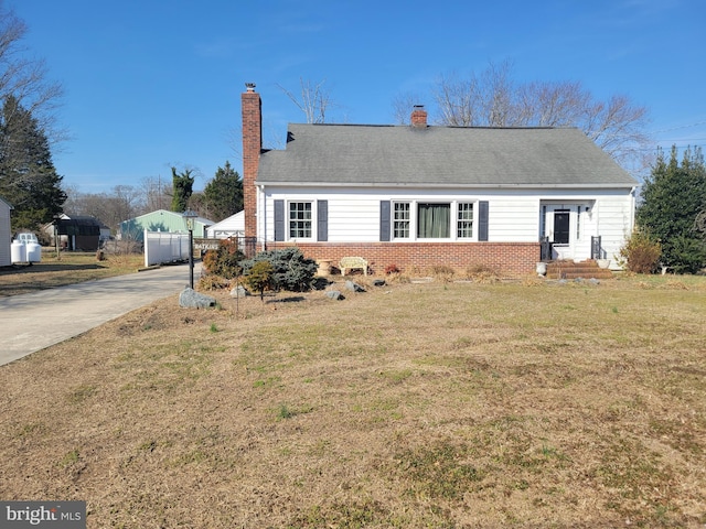 view of front facade featuring brick siding, a front lawn, fence, a chimney, and driveway