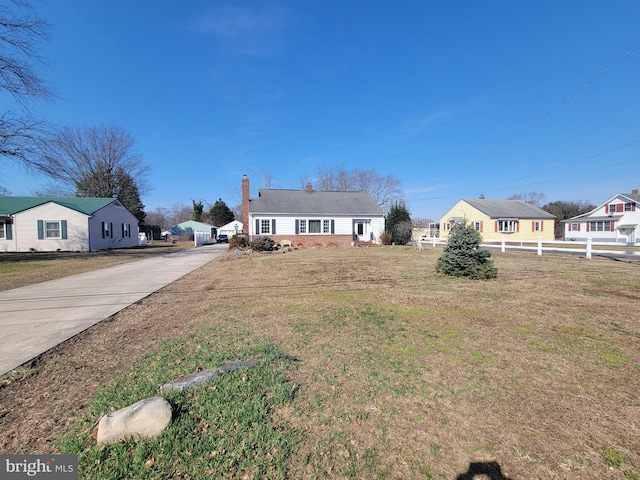 view of front of home featuring a front lawn, concrete driveway, fence, and a chimney