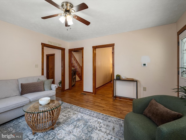 living area featuring a textured ceiling, wood finished floors, baseboards, and ceiling fan