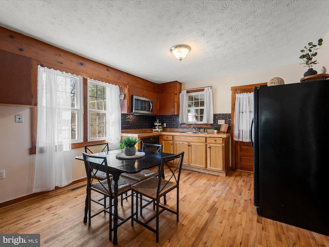 kitchen with light wood-style flooring, a sink, stainless steel microwave, backsplash, and freestanding refrigerator