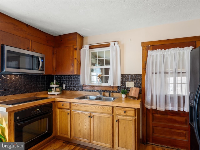 kitchen with backsplash, black appliances, light countertops, a textured ceiling, and a sink