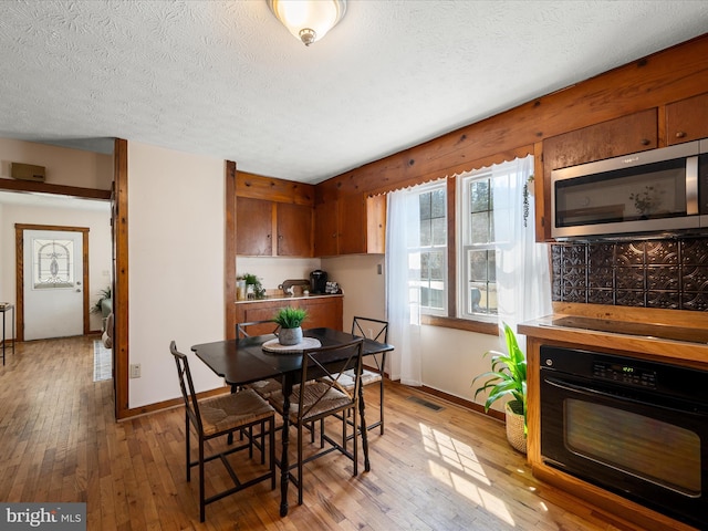 dining area featuring visible vents, baseboards, a textured ceiling, and light wood finished floors