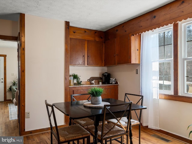 dining area with a textured ceiling, baseboards, visible vents, and light wood-type flooring