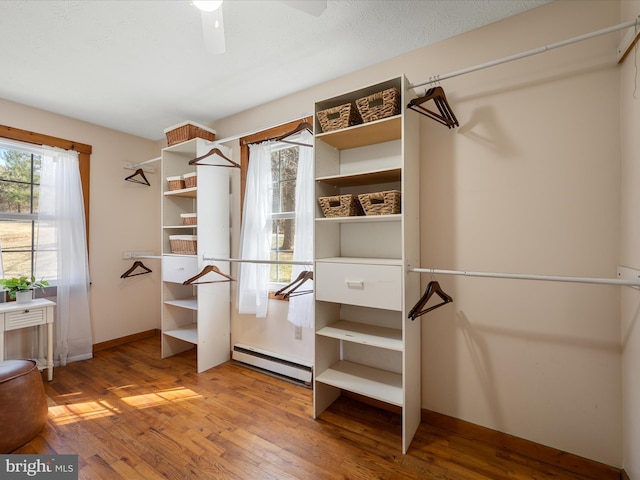 walk in closet with a baseboard heating unit, ceiling fan, and wood-type flooring