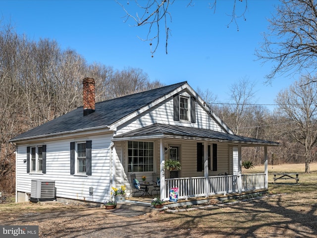 farmhouse-style home featuring central air condition unit, covered porch, a chimney, metal roof, and a standing seam roof