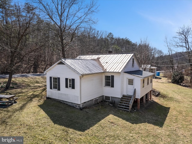 rear view of property with a forest view, entry steps, a lawn, metal roof, and a standing seam roof