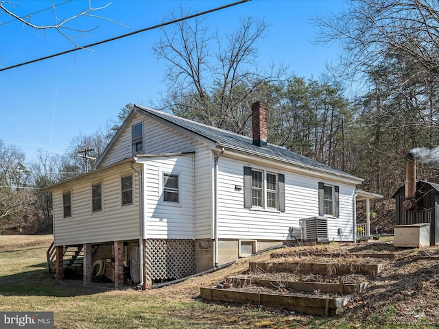 back of property with cooling unit, a vegetable garden, a chimney, a lawn, and metal roof