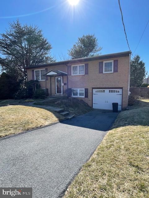 raised ranch with a front yard, a garage, brick siding, and driveway