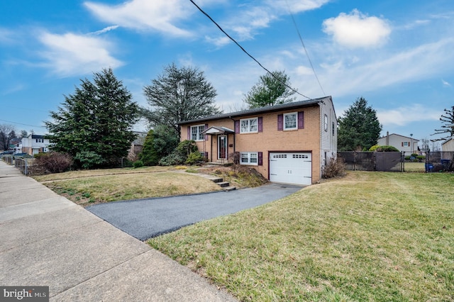 raised ranch with driveway, fence, a front yard, an attached garage, and brick siding