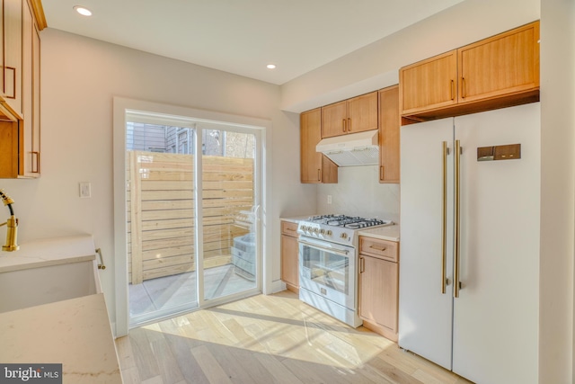 kitchen featuring light wood finished floors, under cabinet range hood, light countertops, high end white refrigerator, and gas stove