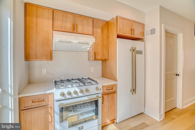 kitchen featuring visible vents, under cabinet range hood, backsplash, white appliances, and light wood finished floors