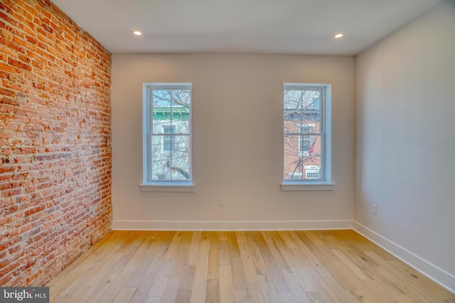 empty room featuring recessed lighting, brick wall, light wood-type flooring, and baseboards