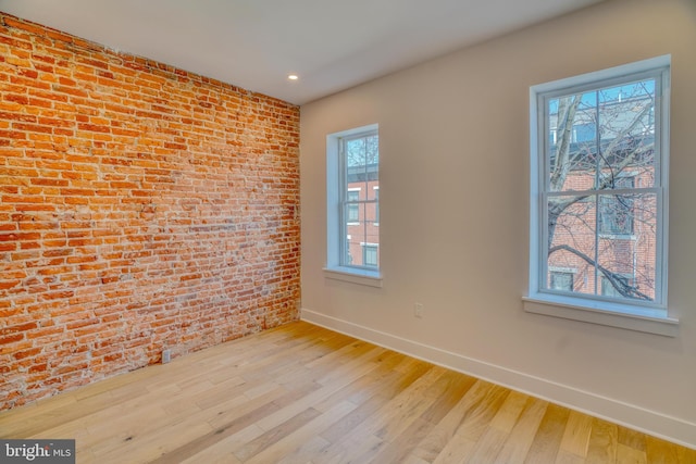 empty room with plenty of natural light, light wood-style floors, baseboards, and brick wall