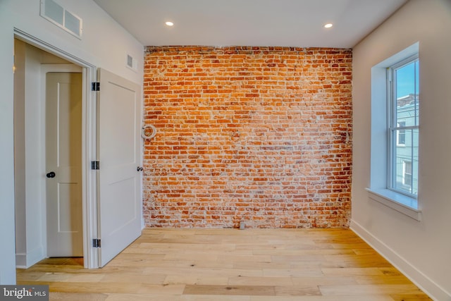 unfurnished room with visible vents, wood finished floors, plenty of natural light, and brick wall