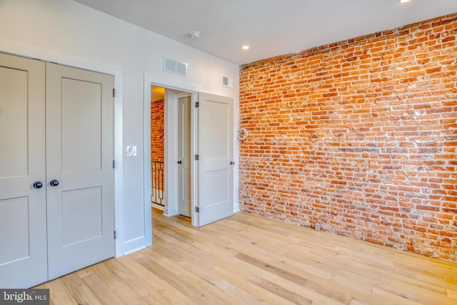 unfurnished bedroom featuring visible vents, wood finished floors, recessed lighting, a closet, and brick wall