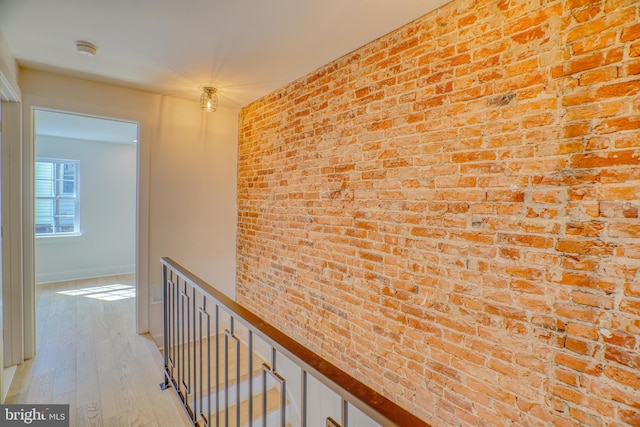 corridor with light wood-style floors, baseboards, and brick wall