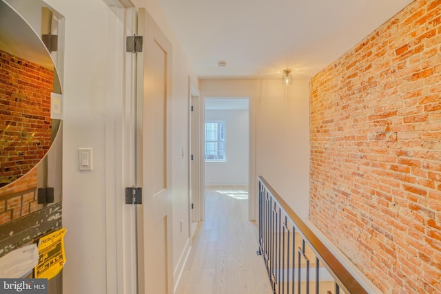 hall featuring light wood finished floors, baseboards, and brick wall