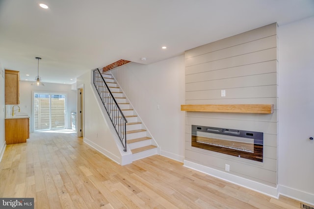 unfurnished living room with stairs, recessed lighting, baseboards, and light wood finished floors