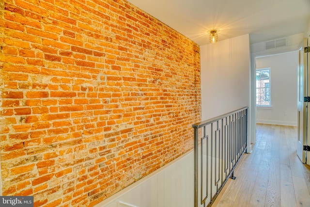 hallway with a wainscoted wall, visible vents, brick wall, light wood-style floors, and an upstairs landing