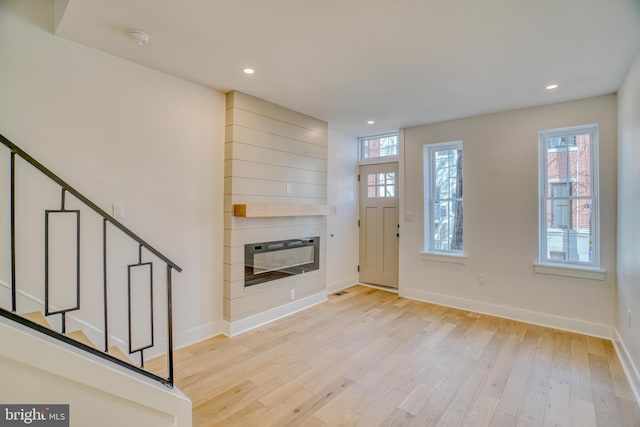 foyer entrance with a large fireplace, light wood-type flooring, stairs, and baseboards