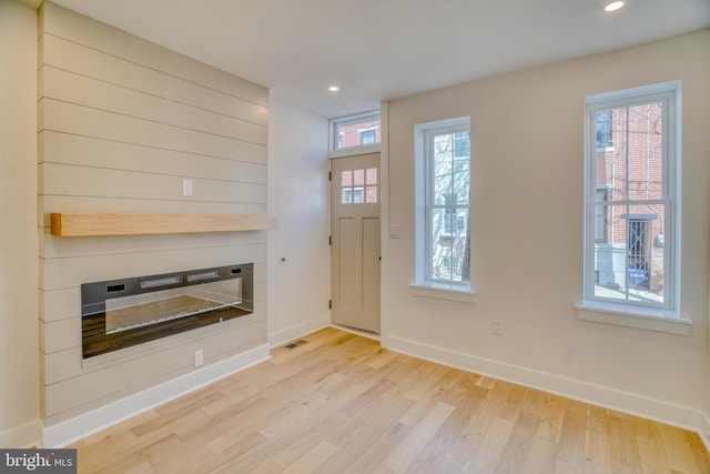 entryway with a glass covered fireplace, a healthy amount of sunlight, light wood-type flooring, and visible vents