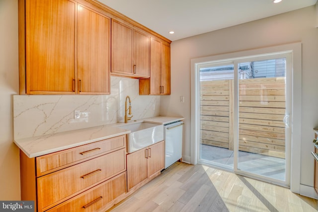 kitchen with a sink, backsplash, light wood-style floors, light stone countertops, and dishwasher