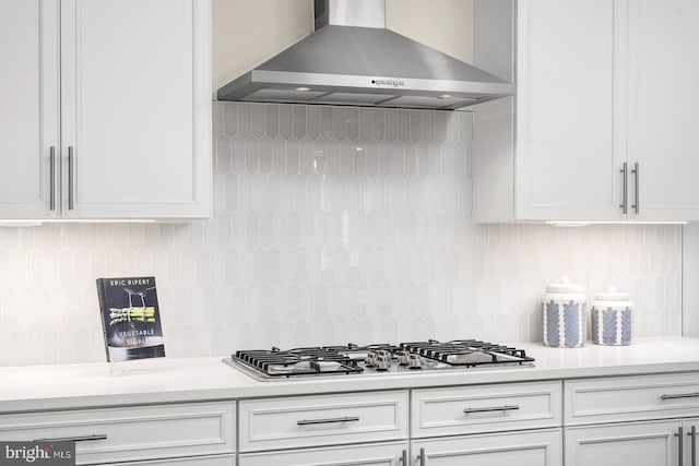 kitchen featuring light countertops, wall chimney range hood, white cabinets, and stainless steel gas cooktop