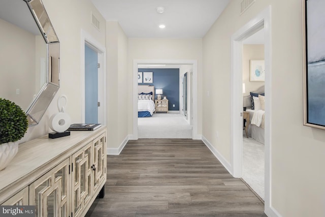 hallway with visible vents, baseboards, and dark wood finished floors