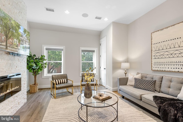 living room featuring visible vents, baseboards, a stone fireplace, recessed lighting, and wood finished floors