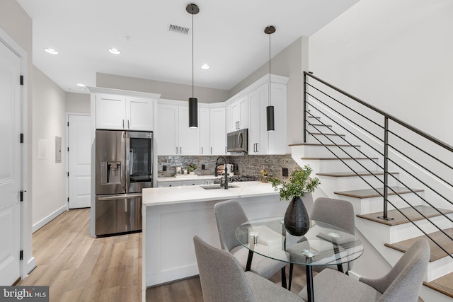 kitchen featuring light wood-style flooring, white cabinetry, stainless steel appliances, a peninsula, and decorative backsplash