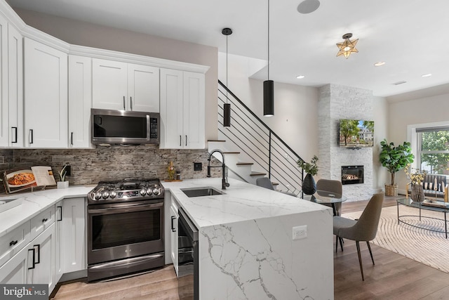 kitchen featuring tasteful backsplash, light wood finished floors, a stone fireplace, appliances with stainless steel finishes, and a sink