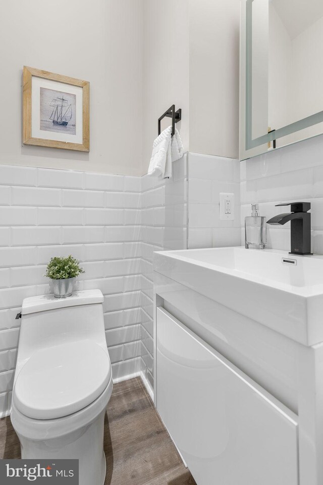 bathroom with toilet, wood finished floors, tile walls, wainscoting, and vanity