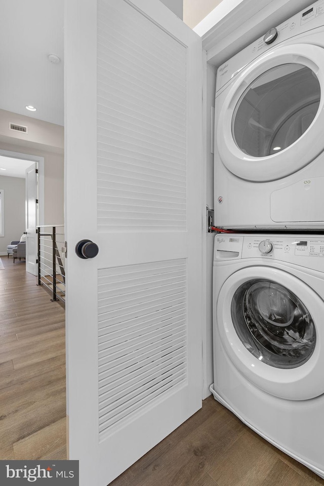 clothes washing area with visible vents, wood finished floors, stacked washing maching and dryer, recessed lighting, and laundry area