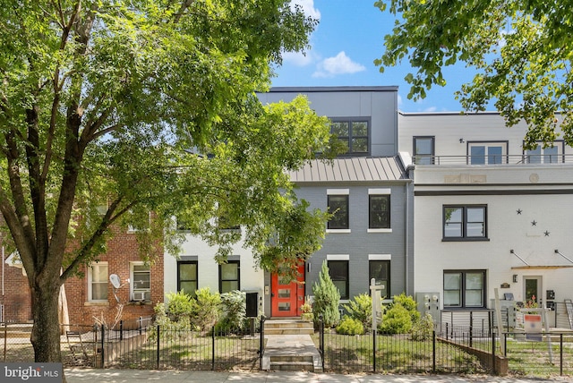 townhome / multi-family property with brick siding, a balcony, metal roof, and a fenced front yard