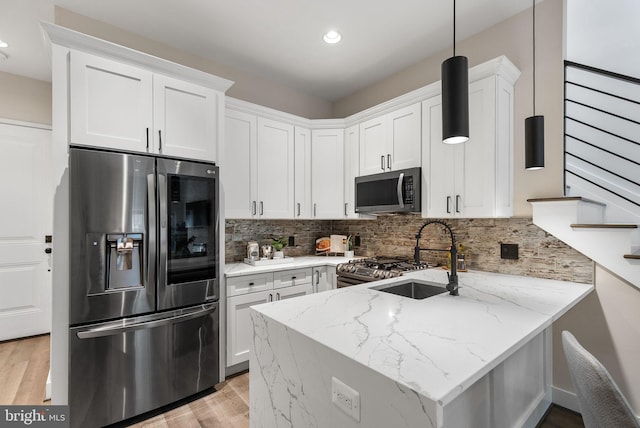 kitchen with light stone counters, a peninsula, a sink, white cabinets, and appliances with stainless steel finishes