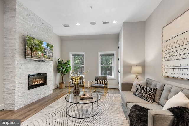 living room with visible vents, a fireplace, baseboards, and wood finished floors