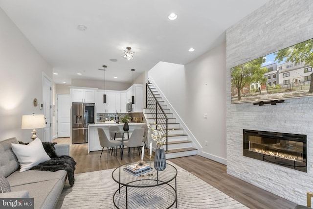 living area with light wood finished floors, a stone fireplace, recessed lighting, and stairs