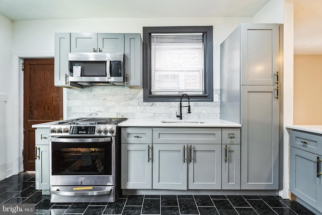 kitchen with tasteful backsplash, gray cabinetry, light countertops, stainless steel appliances, and a sink