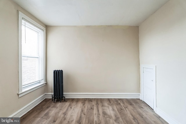 unfurnished room with wood finished floors, radiator heating unit, baseboards, and plenty of natural light