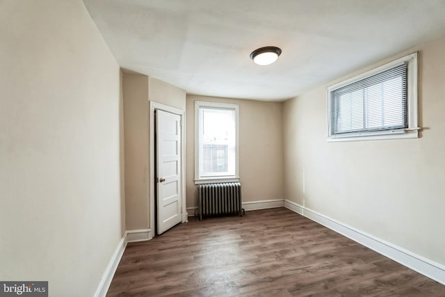 empty room featuring baseboards, radiator heating unit, and dark wood-type flooring