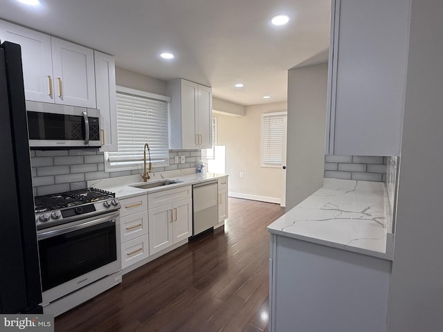 kitchen with a sink, stainless steel appliances, light stone counters, and white cabinets