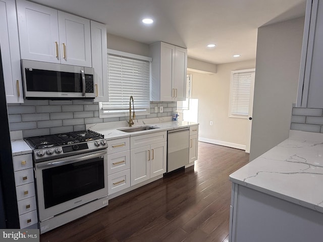 kitchen with light stone counters, dark wood-style floors, a sink, appliances with stainless steel finishes, and backsplash